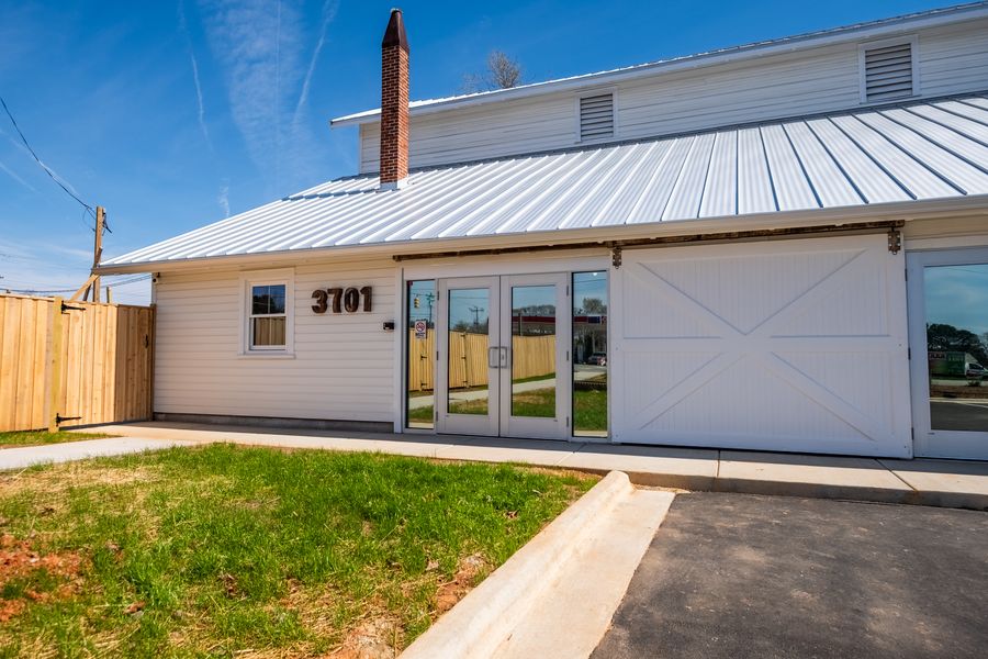 The entrance to the school: white siding with the numerals 3701, a sliding barn door beside a set of glass double doors, and a cedar privacy fence.