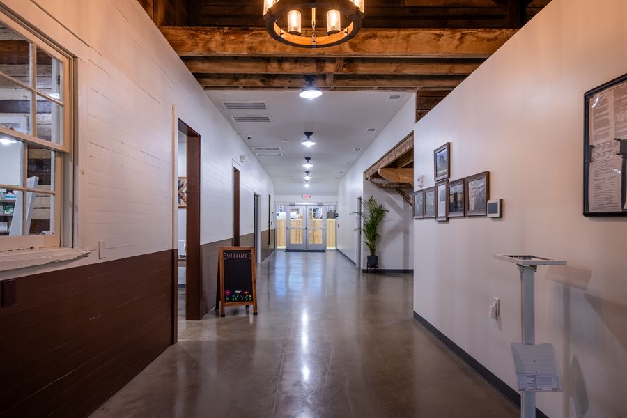 A restored hallway with original painted board walls, a chalkboard welcome sign, framed restoration photographs and a polished concrete floor running to glazed doors at the far end.