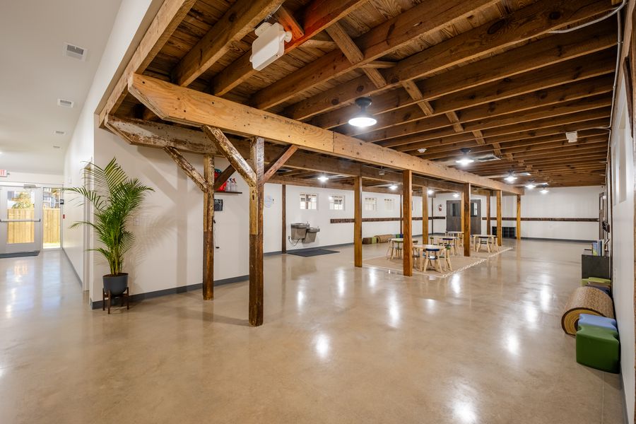 A wide view along the common area showing the repeated timber posts and beams, coat hooks along the wall, rolled mats and low seating.