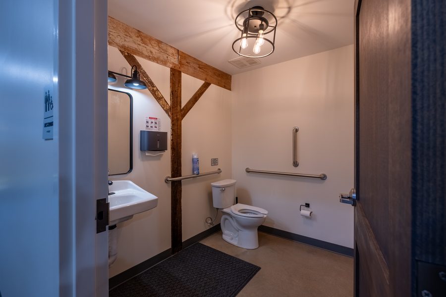 An accessible restroom with a wall-hung sink, mirror, grab bars and an original timber post and brace left exposed against the white wall.
