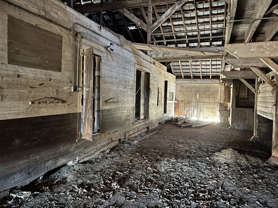 The upper level of the barn: exposed rafters and purlins, boarded openings in the gable wall, and a plank floor.