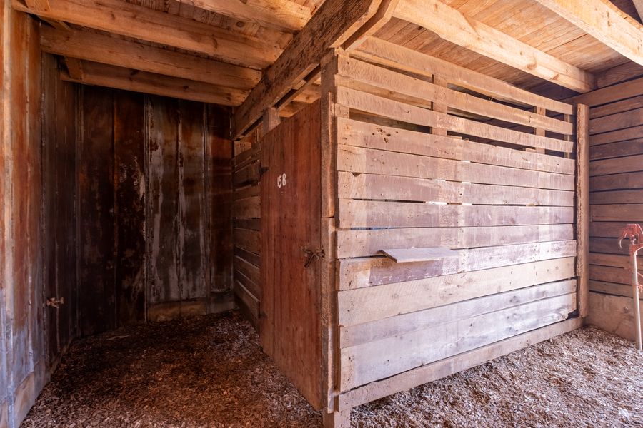 A stalls area of the original barn with rough-sawn timber posts and beams, weathered board partitions, rusted metal sheeting and wood-chip flooring.
