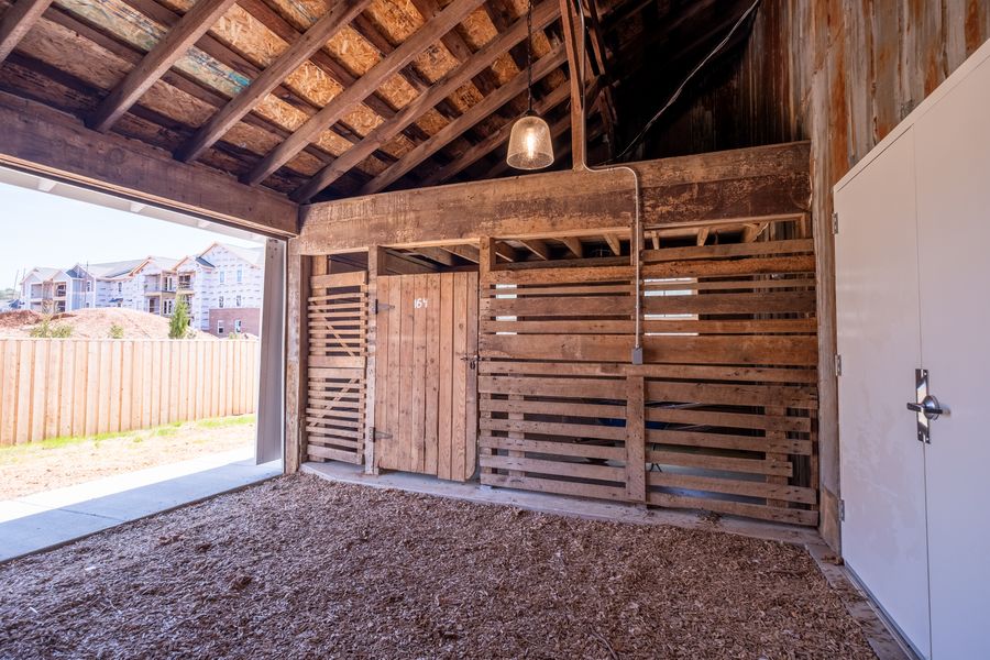A covered open bay of the original structure with exposed rafters, board walls, a pendant light and wood-chip flooring, opening onto the fenced yard.