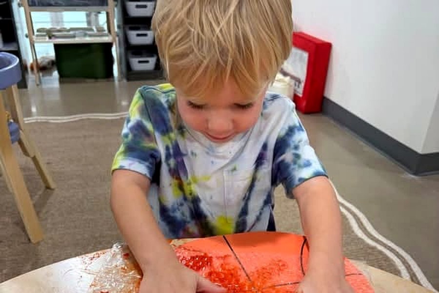 A young child pressing both hands into orange paint spread over bubble wrap on a table, mid-print.